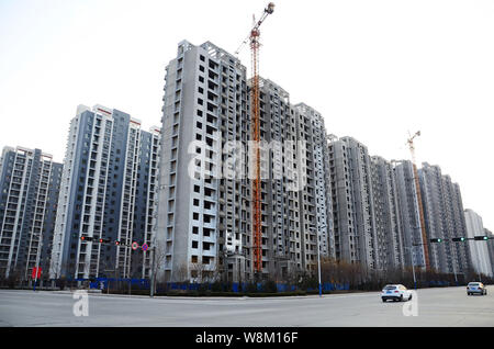 --FILE--Cars pass by new high-rise residential property project under construction in Binzhou city, east China's Shandong province, 4 February 2016. Stock Photo