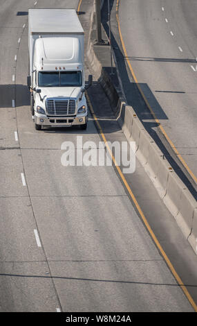 Big rig white long haul bonnet professional heavy-duty semi truck transporting commercial cargo in dry van semi trailer for delivery driving on the le Stock Photo