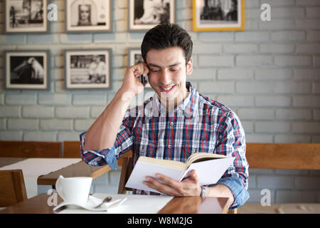 Young man talking on a mobile phone and reading a book in a restaurant Stock Photo