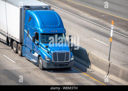 Big rig blue long haul bonnet professional heavy-duty semi truck transporting commercial cargo in dry van semi trailer for delivery driving on the lef Stock Photo
