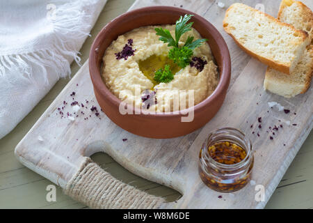 A close-up of a colorful snack composition on a wooden background. Delicious hummus in glass bowl and on a wooden plate. Stock Photo