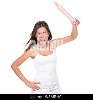 Crazy upset housewife or chef woman holding up a rolling pin in anger threatening to hit in violence, isolated on white studio background. Funny negative expression Asian girl screaming at camera. Stock Photo