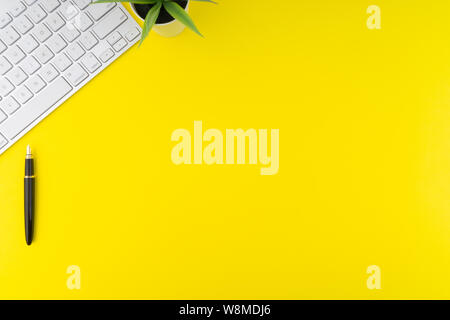 Flat lay view of office table desk. Workspace with keyboard, black pen and decoration flower on yellow background. Business and Copy Space concept Stock Photo