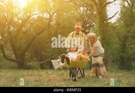 Grandma And Grandpa Are Pushing Their Grandchildren In A Wheelbarrow3 Stock Photo