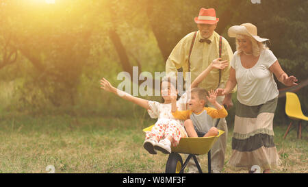 Grandma and grandpa are pushing their grandchildren in a wheelbarrow2 Stock Photo