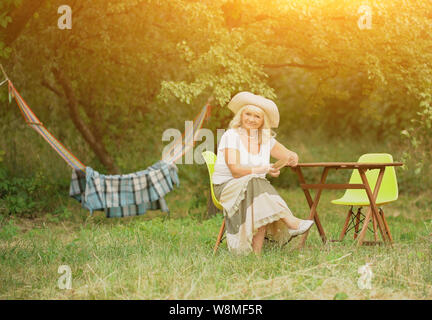 The old lady is sitting in the garden near the hammock. Stock Photo