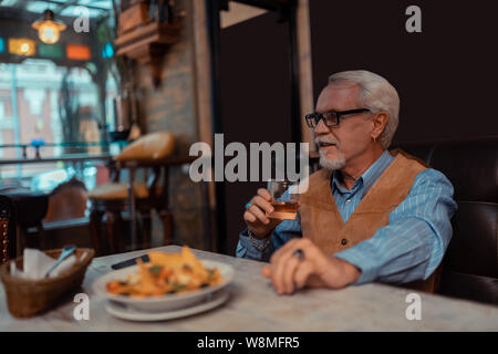 Grey-haired bearded man eating salad and drinking whisky Stock Photo