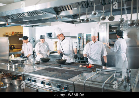 Five chefs wearing uniforms posing in a kitchen. Stock Photo