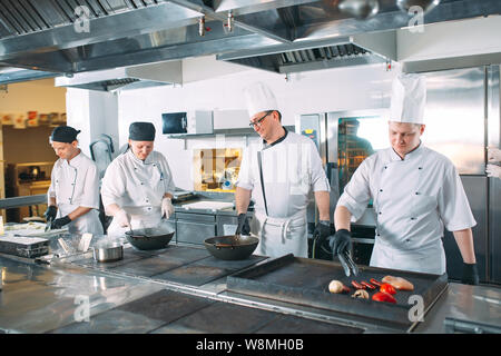 Five chefs wearing uniforms posing in a kitchen Stock Photo