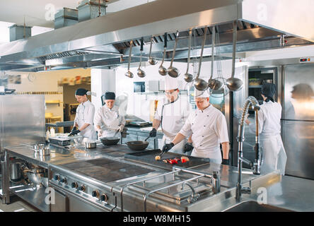 Five chefs wearing uniforms posing in a kitchen. Stock Photo