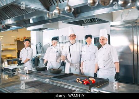 Five chefs wearing uniforms posing in a kitchen. Stock Photo