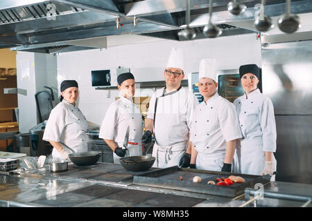 Five chefs wearing uniforms posing in a kitchen. Stock Photo