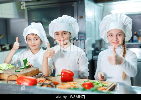 Children in chef's hat grind vegetables on the kitchen. Stock Photo