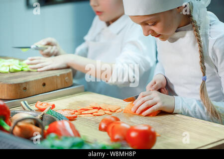 Children in chef's hat grind vegetables on the kitchen. Stock Photo