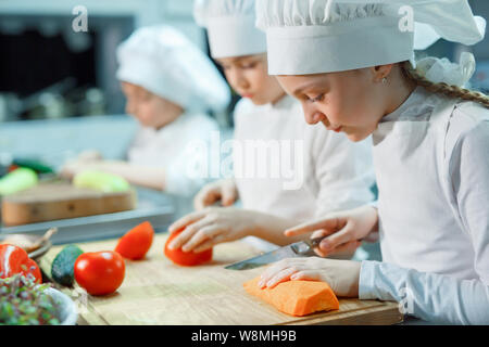 Children in chef's hat grind vegetables on the kitchen. Stock Photo