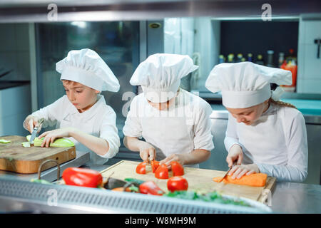 Children in chef's hat grind vegetables on the kitchen. Stock Photo