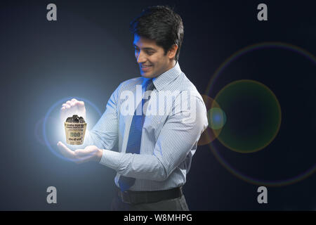 Businessman holding a cup made of 500 rupee note and filled with coins Stock Photo