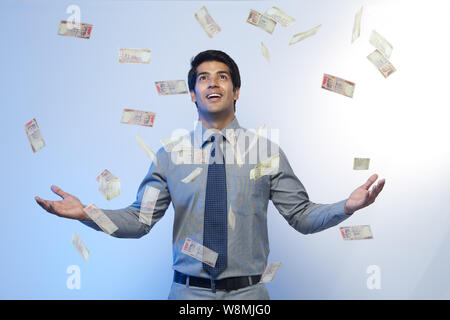 Money falling on a businessman standing with his arms outstretched Stock Photo