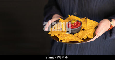 Hands holding plate with Mexican nachos and red chilli sauce.Lifestyle Street food background for banner. Stock Photo