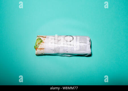 Flat lay photo of tortilla wrapped in newspaper type paper isolated on bright blue background Stock Photo