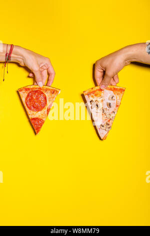 Two hands holding two slices of pizza against yellow background Stock Photo