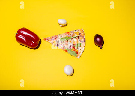 Flat lay photo of pizza slice and vegetables placed around isolated on yellow background Stock Photo