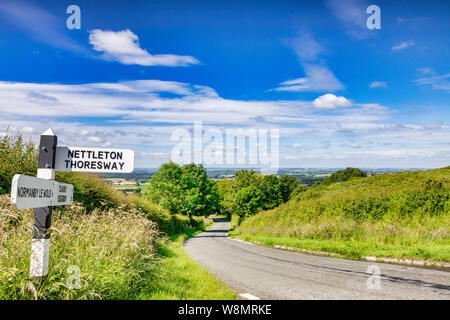 A country road running through the Lincolnshire Wolds, an area of outstanding natural beauty, and a signpost to Nettleton Thoresway. Stock Photo