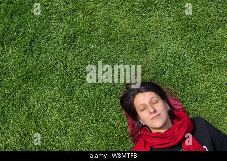 Portrait of a young woman dreaming on a green grass with closed eyes Stock Photo