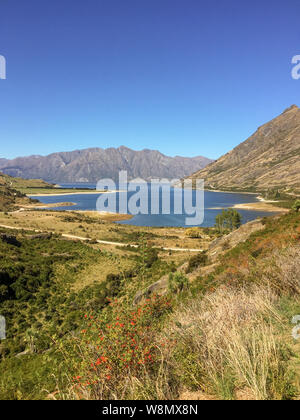 A portrait view of  sparkling waters of a Lake Hawea in Otago, New Zealand, surrounded by jagged mountain peaks against a clear blue sky, nobody in th Stock Photo