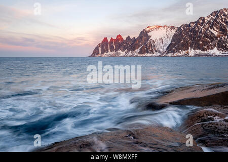 View over colorful rocks and waves to snowy Oksen mountains on a arctic evening , Tungeneset Devils jaw Senja Norway Stock Photo