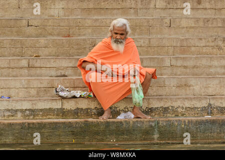 An Indian holy man (sadhu or saddhu) sits on steps on the banks of the Ganges river in Varanasi, Uttar Pradesh, India, South Asia. Stock Photo