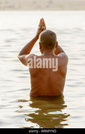 An Indian man offers morning prayers to the gods in the River Ganges at Varanasi, Uttar Pradesh, India, South Asia. Stock Photo