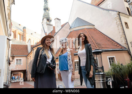 Three traveling girl friends with light backpacks walking exploring Riga city - Travel tourism concept after transfer from airport - Wearing hats and Stock Photo