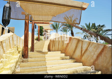 Outdoor stairway with a sun tent. In the background there are palm trees and fountain jets of water. A typical Arab lamp is hanging. Stock Photo