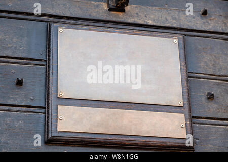 Closeup vintage rectangular shape metal iron copper golden aged plate, nameboard on a dark brown wooden wall. Concept place for lettering, text, copys Stock Photo
