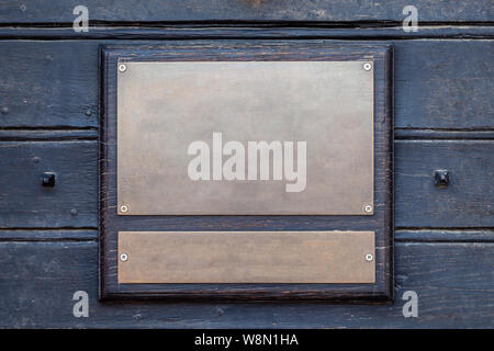 Closeup vintage rectangular shape metal iron copper golden aged plate, nameboard on a dark brown wooden wall. Concept place for lettering, text, copys Stock Photo