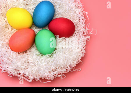 Five Easter colored eggs lie in the nest on a gently pink background, top view. Horizontal photo. Stock Photo