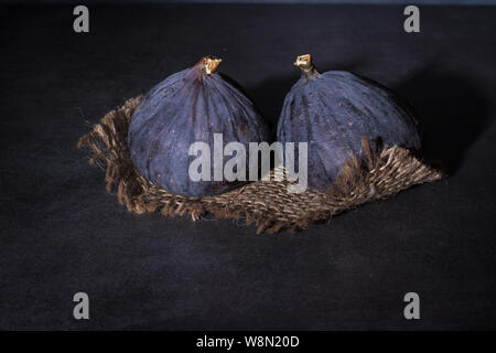 Two ripe purple figs lie on coarse cloth and on a concrete top. Stock Photo