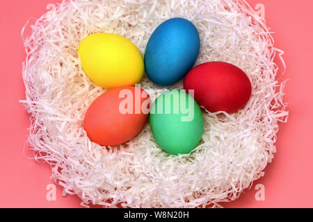 Five Easter colored eggs lie in the nest in the center on a gently pink background, top view. From the nest is falling hard the shadows. Horizontal ph Stock Photo