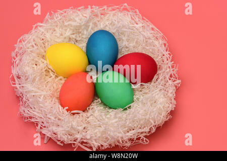 Five Easter colored eggs lie in the nest on a gently pink background, top view. Horizontal photo. Stock Photo