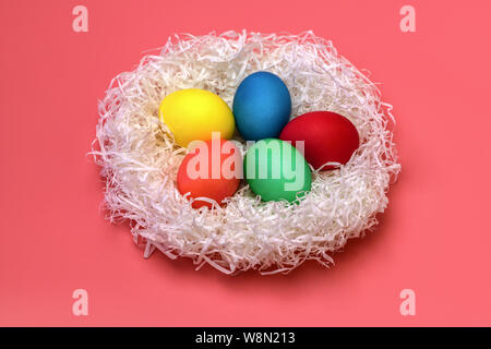 Five Easter colored eggs lie in the nest in the center on a gently pink background, top view. From the nest is falling hard the shadows. Horizontal ph Stock Photo