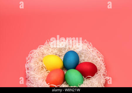Five Easter colored eggs lie in the nest at the bottom on a soft pink background, on top there is a place for the inscription. Horizontal photo. Stock Photo