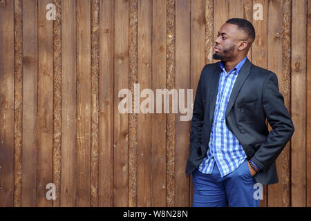 Portrait of young black bearded guy standing and hand in pocket. Afro american man in suit is confident and looks away on dark wood background, copy space Stock Photo