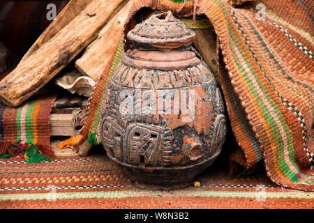 An ancient oriental ceramic jug with ornament on the market square stands on woven ethnic brown carpets and wooden firewood Stock Photo