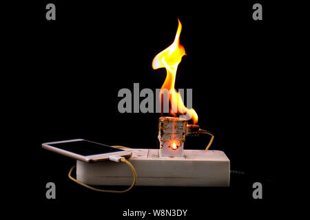 On fire Adapter smart phone charger at plug in power outlet at black background Stock Photo