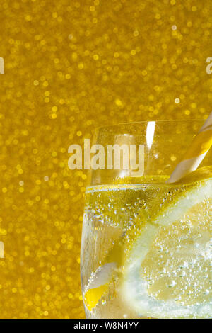 fresh soda with bubles an ice cube, a  slice of lemon and a straw on a shiny golden background, free space for text Stock Photo