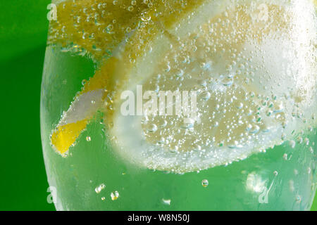 fresh drink with bubles an ice cube, a  slice of lemon and a straw on a green background Stock Photo
