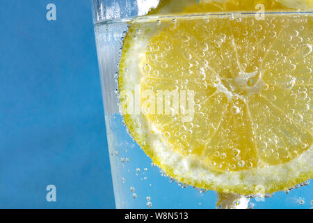 fresh drink with bubles an ice cube, a  slice of lemon and a straw on a blue background Stock Photo