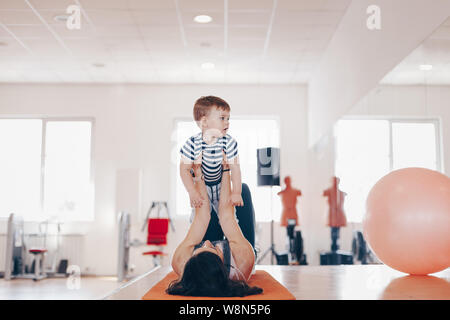 Portrait of happy  young fit mother doing exercise at gym and having fun with her baby boy. Concept of healthy living.  Sport, motherhood and active c Stock Photo