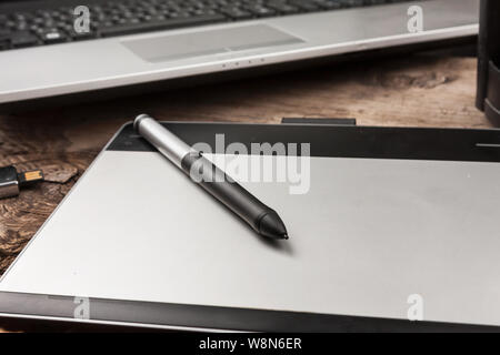 Close-up shot of graphics tablet with stylus on the background of a laptop. Essential tools for graphic designer. Professional retoucher equipment. De Stock Photo